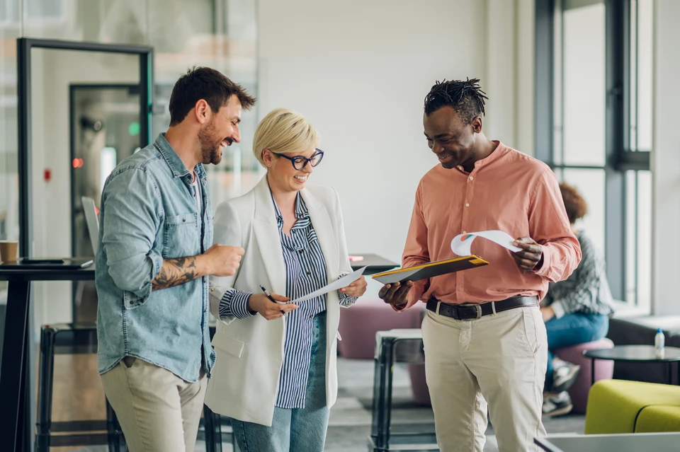 Divers collègues d'affaires discutant des documents utilisés pour accompagner la réunion mensuelle de l'entreprise, des gens d'affaires multidisciplinaires discutant du rapport de vente annuel de l'entreprise aux participants